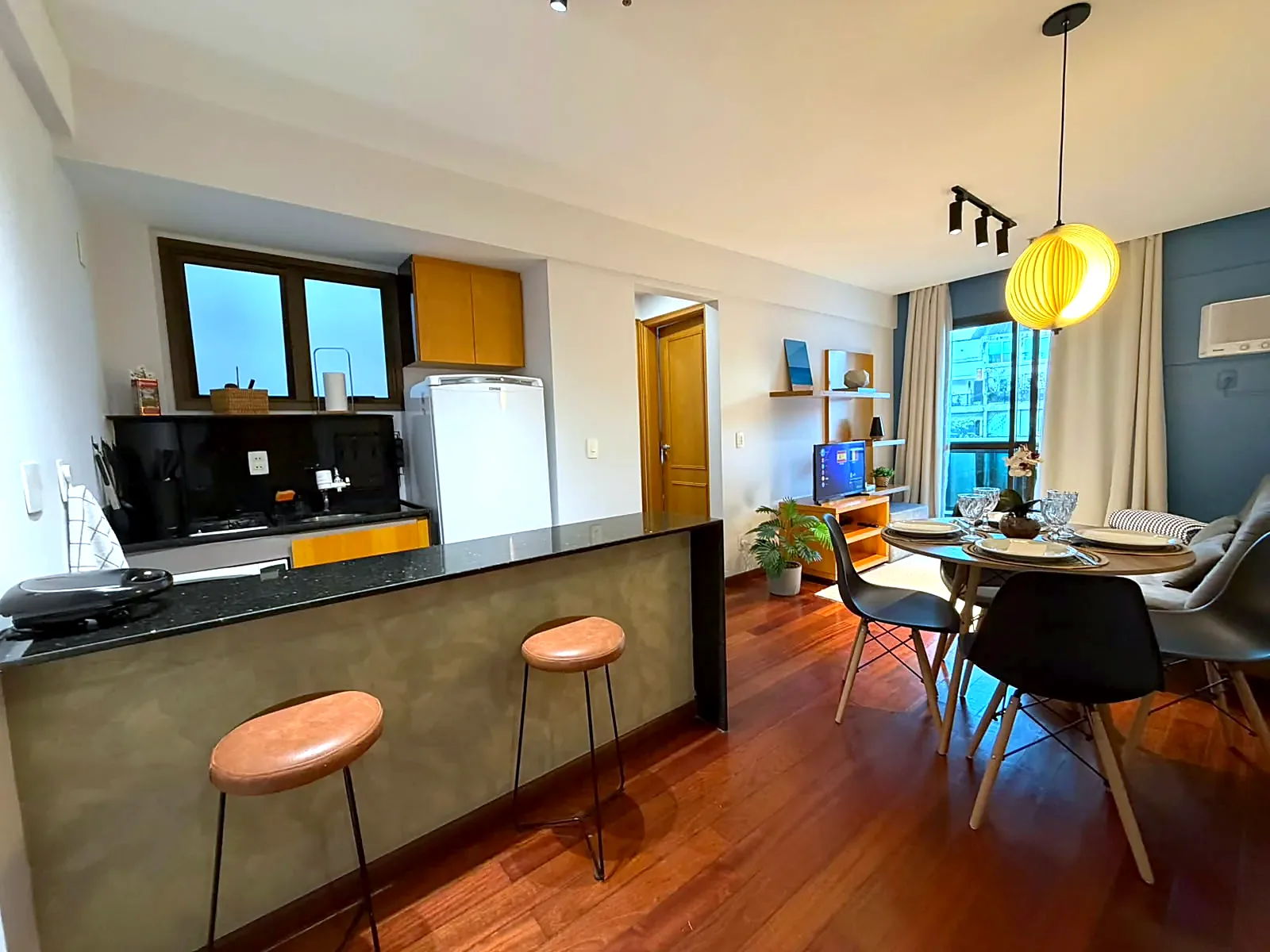 Cozinha integrada com bancada e banquetas, sala de jantar e varanda do flat em Ipanema